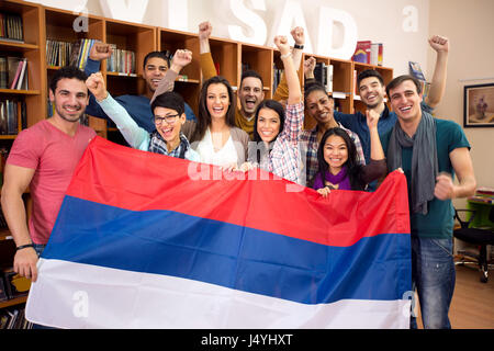Glückliche Gruppe von Studenten aus Serbien mit erhöhten Sieg Fäusten, präsentiert ihr Land mit Flagge Stockfoto