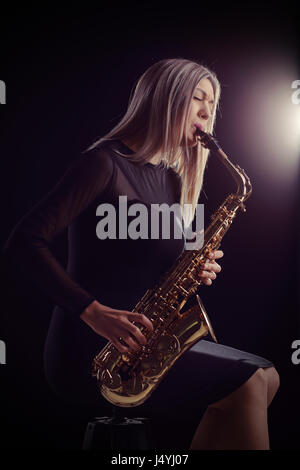 Jazzmusikerin auf einem Stuhl sitzend und ein Saxophon zu spielen, während eines Konzerts Stockfoto