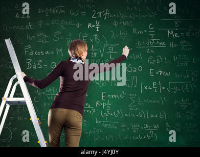 Studentin auf einer Leiter und schreibt auf einer Kreidetafel Stockfoto