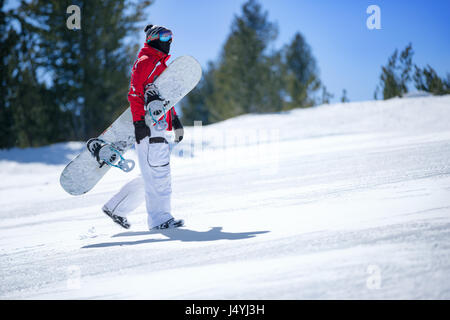 Snowboarder hält snowboard und steigt den Hang hinauf Stockfoto