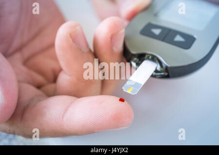 Nahaufnahme eines männlichen Finger mit Blut Tropfen und Blutzuckermessgerät Teststreifen Stockfoto