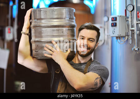 Männliche Brauer mit ein Metall Bierfass auf dem Hintergrund der Brauerei Stockfoto