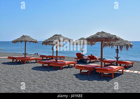 Touristischen ruht auf Sonnenliegen unter Stroh Sonnenschirmen in Perissa, Santorin, Kykladen, Griechenland Stockfoto