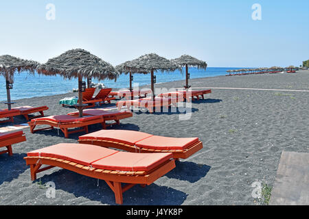 Touristischen ruht auf Sonnenliegen unter Stroh Sonnenschirmen in Perissa, Santorin, Kykladen, Griechenland Stockfoto