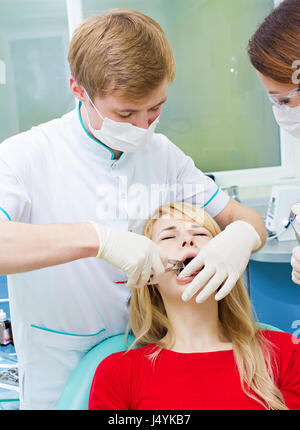 Closeup junge Frau am Zahnarztpraxis Klinik. Männlichen Arzt und Assistentin Extraktionsverfahren mit Pinzette entfernen Patienten Zahn durchführen. Healthcar Stockfoto