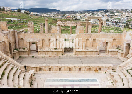 Römisches Theater in Jerash, Jordanien mit Anzeigen der Stadt hinter der Bühne ich und bewölkten Himmel. Der Boden des Theaters hat einen Mosaikboden. Stockfoto