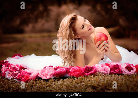 Schöne Braut mit blonden Haaren im weißen Kleid mit rosa und roten Rosenblüten, Park-Outdoor-Hochzeit-Foto-Session, Mode Schönheit und Stil Stockfoto