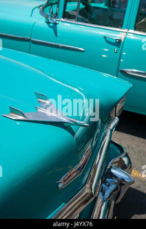 Havanna - ca. Juni 2011: Die Kühlerfigur von 1953 Chevrolet BelAir schimmert in der tropischen Sonne neben einem anderen amerikanischen Oldtimer in blauen Farbtönen. Stockfoto
