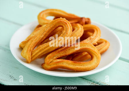 Nahaufnahme von einigen Churros typisch für Spanien auf einem weißen Keramik Teller platziert auf einem blassen Grün rustikalen Holztisch Stockfoto