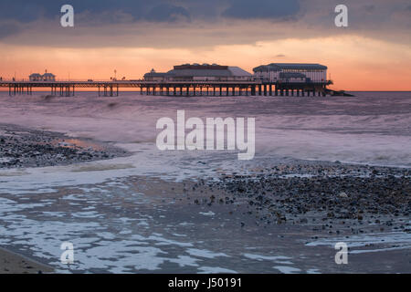 Cromer Pier in einem Sommergewitter mit Wellen und Brandung hämmerte den Kiesstrand Stockfoto