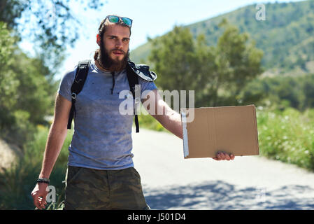Trampen Reisenden mit einem leeren Pappschild auf einer Bergstraße. Billig reisen. Auto-Stopp Stockfoto