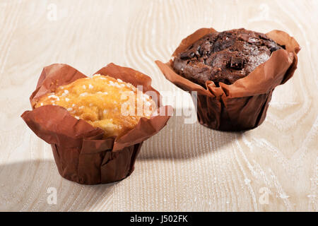 Zwei frisch gebackene Muffins oder Cupcakes, einer Schokolade und einem Vanille, nebeneinander auf einem Holztisch in einem Konzept von zu Hause backen, eine Bäckerei oder nutritio Stockfoto