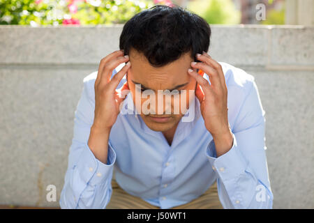 Closeup Portrait, gestresste junge Geschäftsmann, Hände am Kopf mit Kopfschmerzen, isolierte Hintergrund grau Bank außerhalb. Negative menschliche Emotion faci Stockfoto