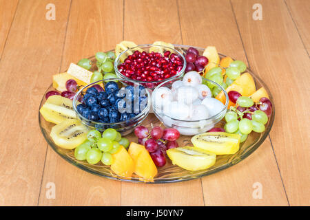 Glaswaage mit verschiedenen frischen Sommerfrüchten auf Holzboden Stockfoto