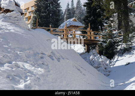 Hölzerne Brücke zwischen alten Holzhütten in einer verschneiten Ski Stadt an einem sonnigen Wintertag Stockfoto