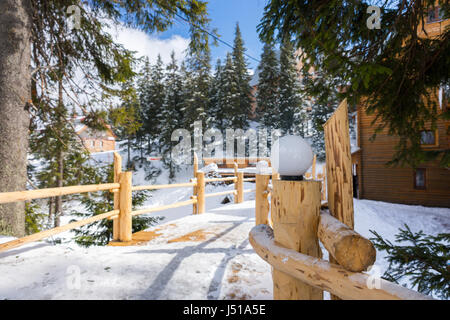 Holzbrücke mit Straßenlaternen zwischen alten Holzhütten in einer verschneiten Ski Stadt an einem sonnigen Wintertag Stockfoto