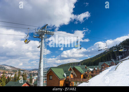 Skilift mit Sitze gehen über den Berg und Holzhütten in einem verschneiten Skigebiet Stockfoto