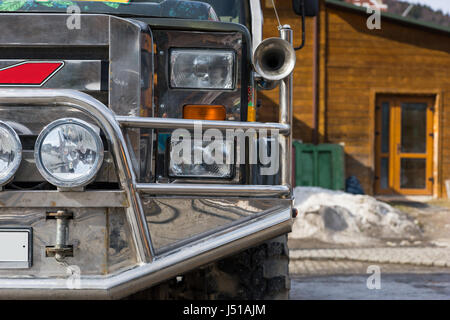 Nahaufnahme der Stoßstange eines Jeeps auf dem Parkplatz neben einem Holzhaus in einem Skigebiet im Winter Stockfoto