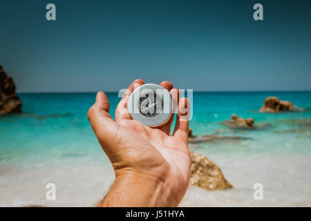 Männliche Hand Holding Kompass am schönen Strand mit dem Meer in türkis-blaue Farbe im Hintergrund Stockfoto