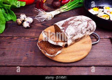 Laib Brot aus Roggenmehl auf einem Brett Küche in der Mitte von frischem Gemüse