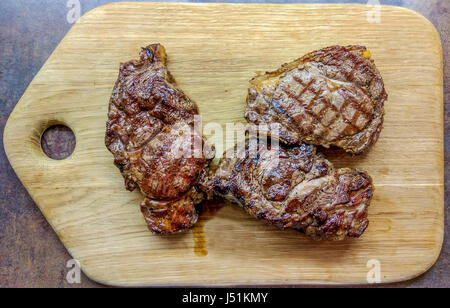 Drei Rib-Eye-Steaks zubereitet auf dem Grill. Sie sind auf dem hölzernen Schreibtisch aus Eiche gefertigt. Stockfoto