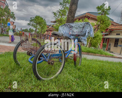 Luodong, Taiwan - 18. Oktober 2016: Ein Dreirad-Fahrrad mit einem rostigen Gepäcktasche lehnte sich gegen einen Baum. Stockfoto