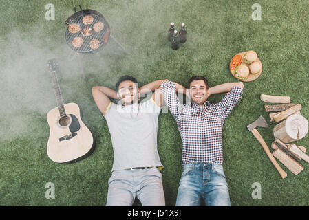 Draufsicht der glückliche junge Männer ruht auf dem Rasen mit Gitarre und Nahrung für Picknick Stockfoto