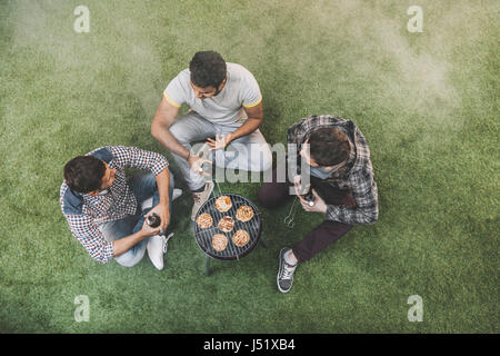 Draufsicht der jungen Männer auf dem Rasen sitzen und trinken Bier und bbq Stockfoto