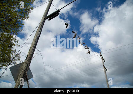 Schuhe und Stiefel aufgereiht auf einem elektrischen Draht über eine Landstraße. Stockfoto