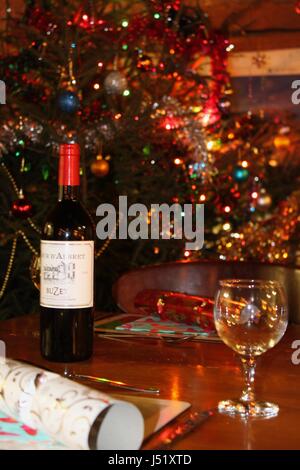 Tabelle für Weihnachtsessen mit Flasche Rotwein, Cracker und leeres Glas und Baum in Backgrond dekoriert Stockfoto
