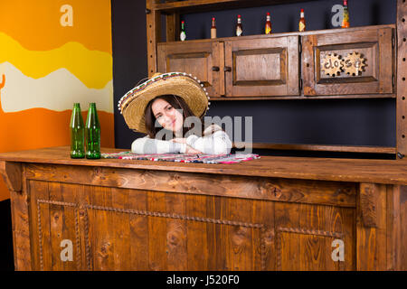 Schöne junge Frau in einen Sombrero stützte sich auf Bartheke mit Bierflaschen in mexikanischen Kneipe Stockfoto