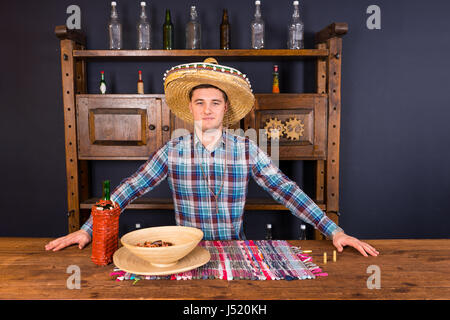 Gut aussehend männlichen Barkeeper im Sombrero stehen an der Theke, Flasche Tequila und eine Platte mit Snacks auf sie in mexikanischen Kneipe Stockfoto