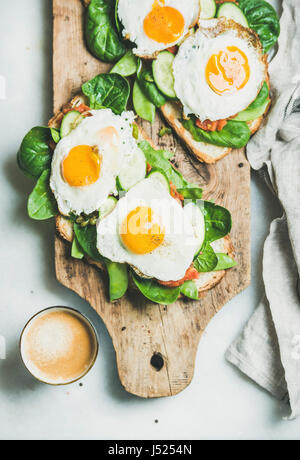 Gesundes Frühstück Sandwiches und Kaffee. Brot-Toast mit Spiegeleiern und frischem Gemüse auf rustikalem Holzbrett über grauem Marmor Hintergrund, Stockfoto