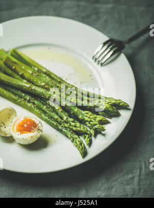 Spargel mit weich gekochtes Ei und Kräutern auf weißen runden Teller über grau Textil Hintergrund, selektiven Fokus gekocht. Sauber essen Food Konzept Stockfoto