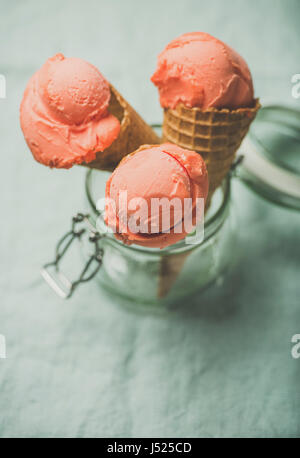 Erfrischende Sommer Blutorange Eis oder Sorbet Kugeln in süße Waffel Kegel im Glas serviert mit frischen Orangenscheibe, leichten grauen Tuch staatlich Stockfoto