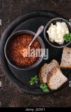 Schale mit rotem Kaviar mit Löffel serviert mit geschnittenem Brot, Butter und Kräutern auf schwarzem Holz Schneidebrett braun Textur Hintergrund. Draufsicht mit s Stockfoto