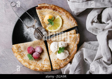 Süße Crêpes Pfannkuchen mit verschiedenen Füllungen frische Himbeeren, Zitroneklumpen, Mascarpone Käse, Minze, Puderzucker mit Vintage Sieb, Textile Leinen o Stockfoto