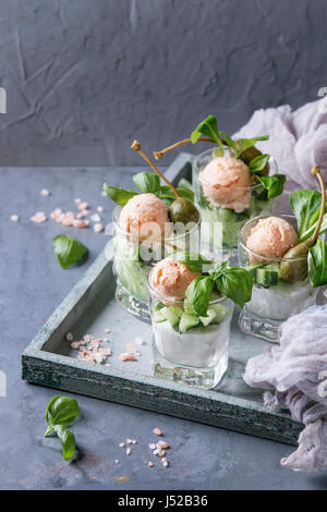 Verrines Vorspeise mit Lachspastete, roter Kaviar, Gurke, Frischkäse, Kräuter, Kapern in Gläsern serviert auf Holztablett mit rosa Salz und Basilikum über Stockfoto