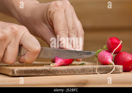 Hände schneiden frische Radieschen auf dem Schneidbrett aus Holz Stockfoto