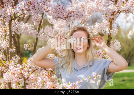 Junge Frau ihre Augen mit frischen bunten Blumen bedecken. Stockfoto