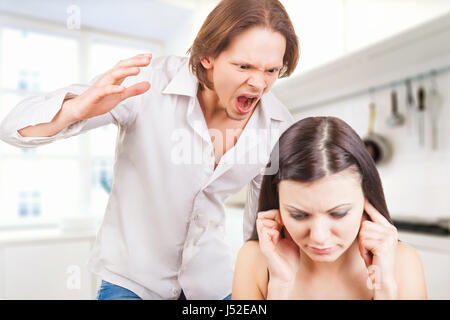 Wütenden Mann schreit die junge Frau in der Küche. Frau für ihre Ohren mit den Händen Stockfoto