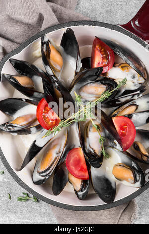 Gekochte Muscheln in einer Pfanne serviert auf einer Serviette, garniert mit Tomaten und Thymian. Gedämpfte Muscheln in Weißweinsauce. Stockfoto