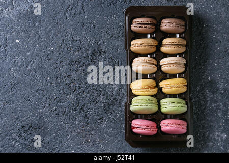 Vielzahl von bunten französische Süßspeise Macaron mit unterschiedlichen Füllungen in Balck Kunststoff-Box über dunkle Stein Textur Hintergrund. Draufsicht mit Raum Stockfoto