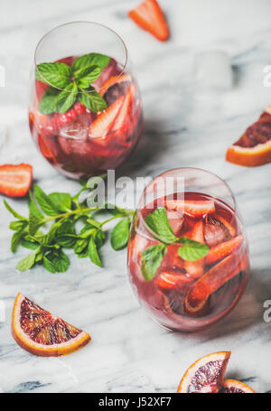 Blutorange und Erdbeere Sommer Sangria. Frucht, erfrischende rose Wein Cocktails in Gläser mit Eis und Minze Blätter über Marmortisch Hintergrund, sel Stockfoto