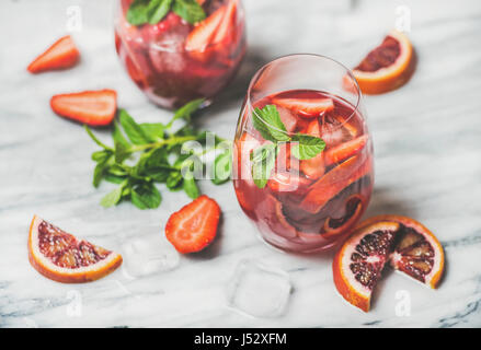 Blutorange und Erdbeere Sommer Sangria. Frucht, erfrischende rose Wein Cocktails in Gläser mit Eis und Minze Blätter über Marmortisch Hintergrund, sel Stockfoto