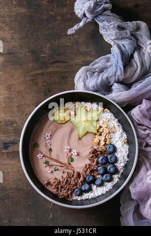 Smoothie Schüssel gesundes Frühstück. Schokolade Joghurt mit Heidelbeeren, Müsli, Kokos, Limette und Karambole auf Textile Gaze über dunklem Holz Textur bac Stockfoto