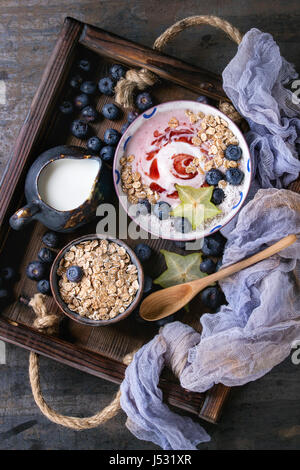 Smoothie Schüssel gesundes Frühstück. Erdbeer-Joghurt mit Müsli, Minze, Heidelbeeren, Krug mit Milch und Karambole in Holztablett auf Textile Gaze über dar Stockfoto