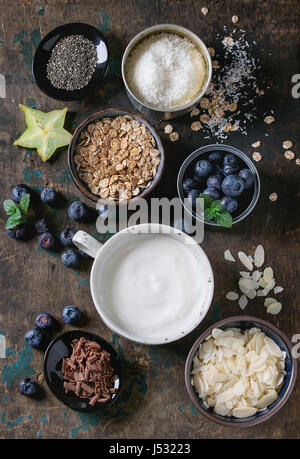 Zutaten für die Herstellung von Smoothies für gesundes Frühstück. Schalen mit Joghurt, Heidelbeeren, Müsli, Mandel Chia-Samen, Kokos, Milch, Schokolade, Minze, caram Stockfoto