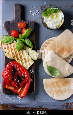 Zutaten für die Herstellung von Pita Brot Brötchen. Gegrilltes Gemüse, Basilikum und Feta-Käse mit Fladenbrot auf hölzernen Portion Brett über graue Textur Rücken Stockfoto