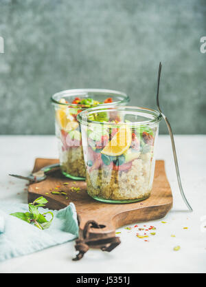 Gesunder Salat mit Quionoa, Avocado, getrockneten Tomaten, Basilikum, frische Minze, Gläser Orange im Glas auf Holzplatte, graue Wand im Hintergrund, selektiven Fokus Stockfoto